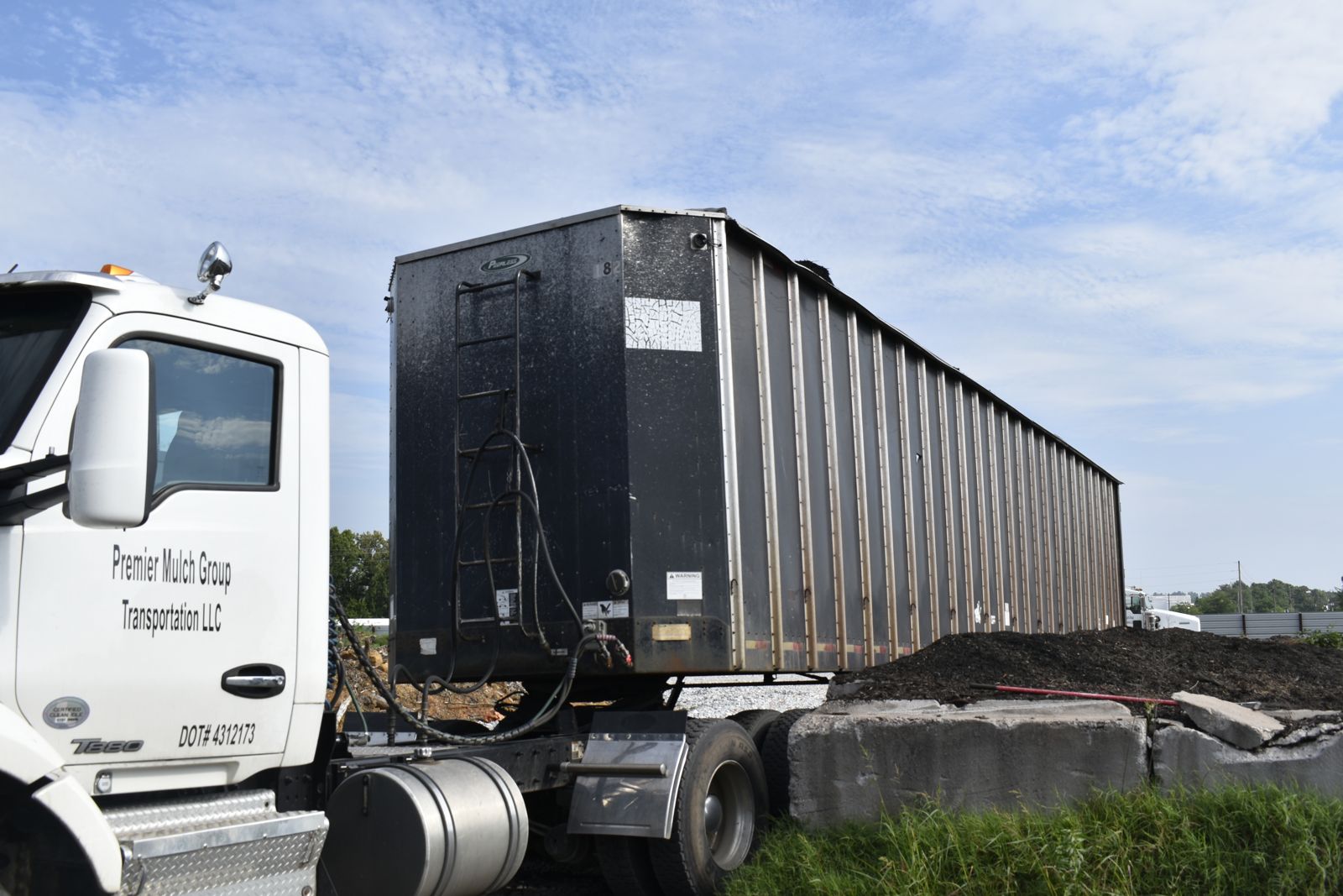 A semi truck with a high-sided bulk trailer parked beside the mulch storage bays at the EWP Mulch yard in Rogers, Arkansas.