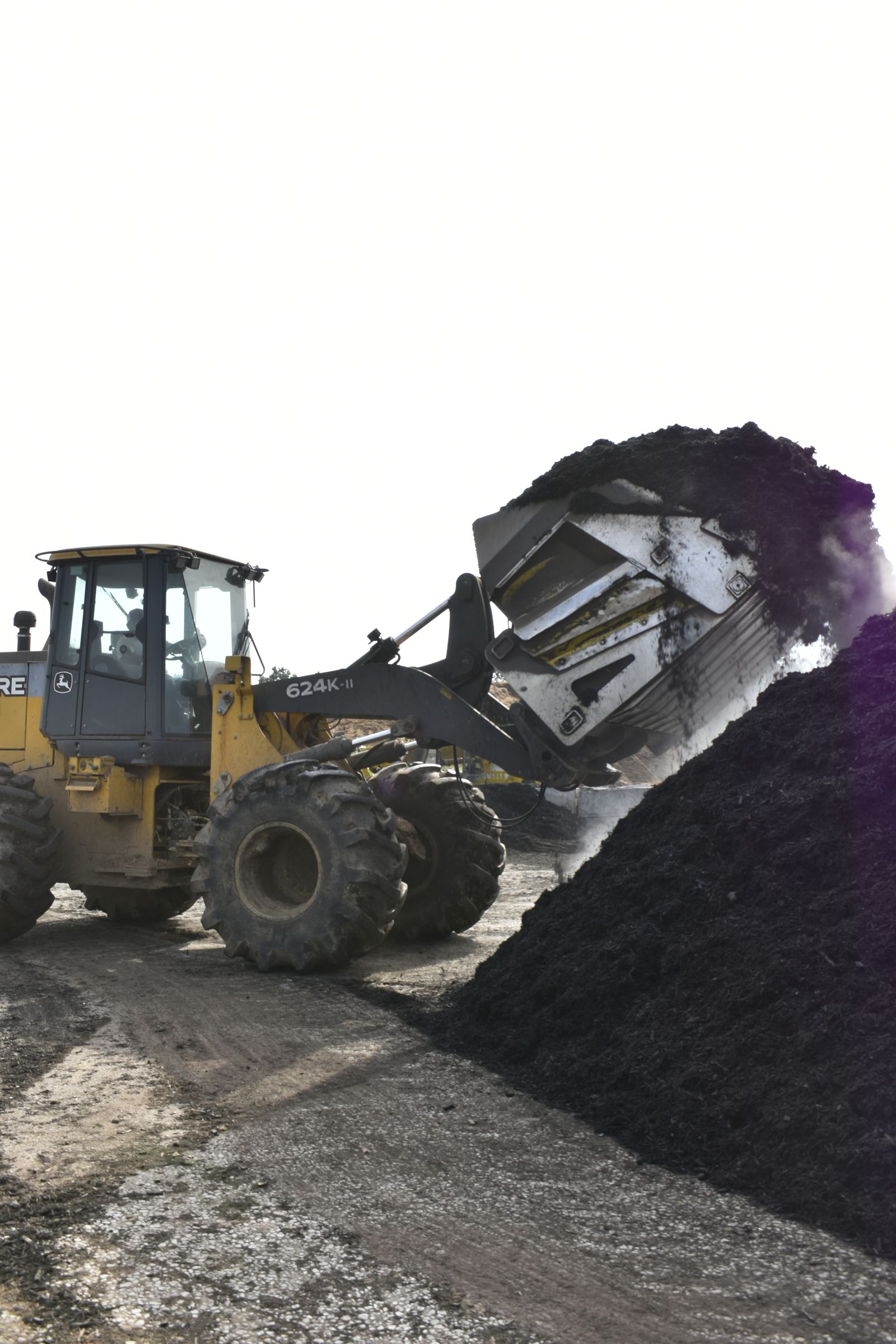 A wheel loader dumps a bucket of black mulch onto a tall pile at the EWP Mulch yard in Rogers, Arkansas.