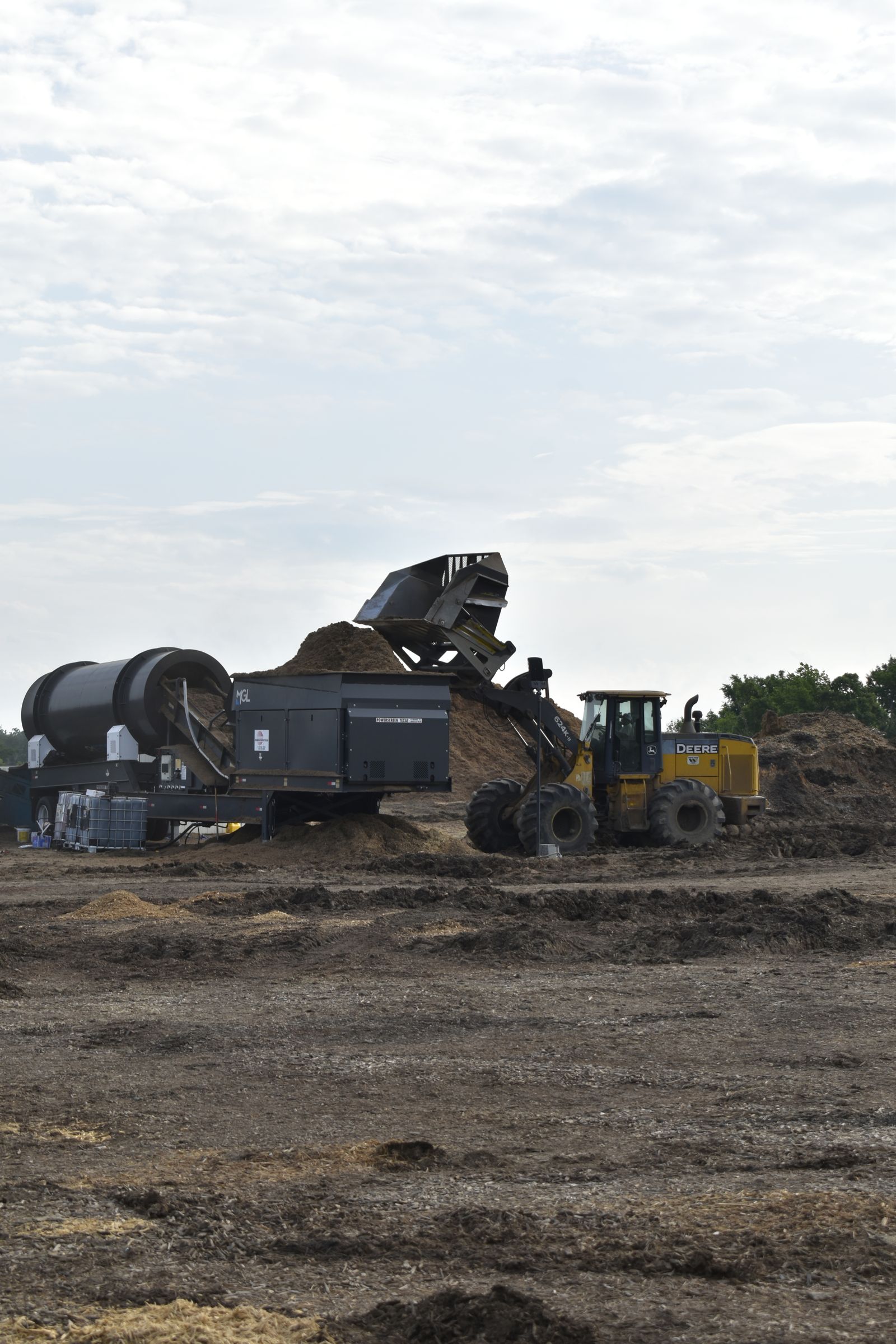A wheel loader tips a bucket of ground wood into the hopper of a trommel screener at the EWP Mulch yard in Rogers, Arkansas.