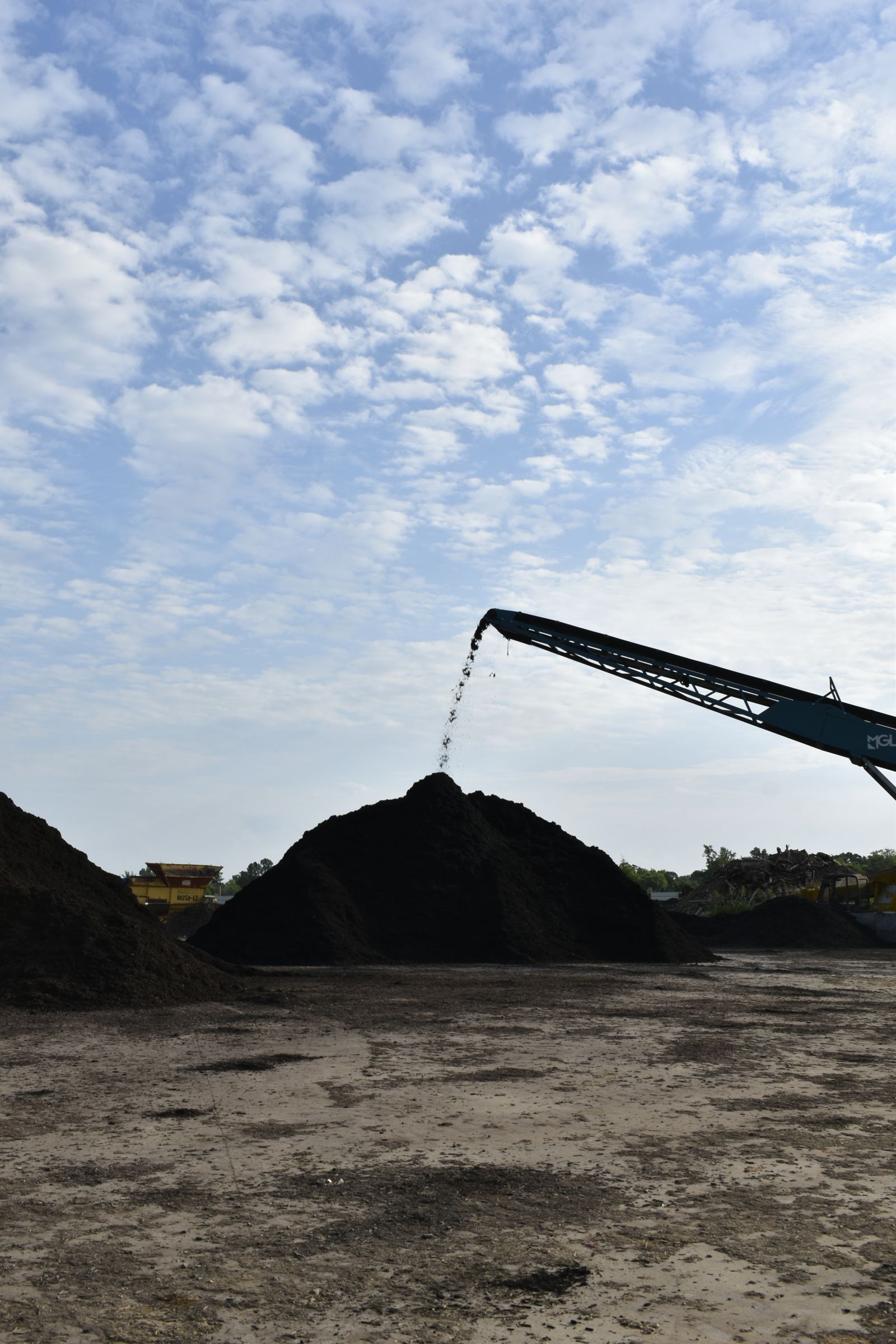 A stacking conveyor pours freshly screened black mulch onto the peak of a tall pile at the EWP Mulch yard in Rogers, Arkansas.