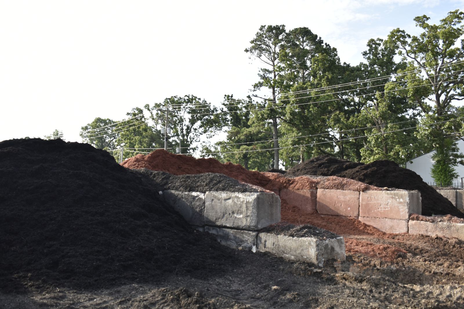 Tall piles of black, red, and dark brown mulch in concrete storage bays at the EWP Mulch yard in Rogers, Arkansas.
